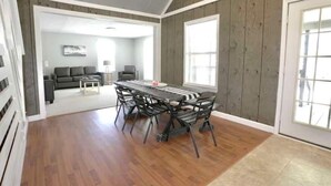 A spacious living room with a dining area, wooden walls, and large windows. - Sugarwood Boathouse (Ten Mile)