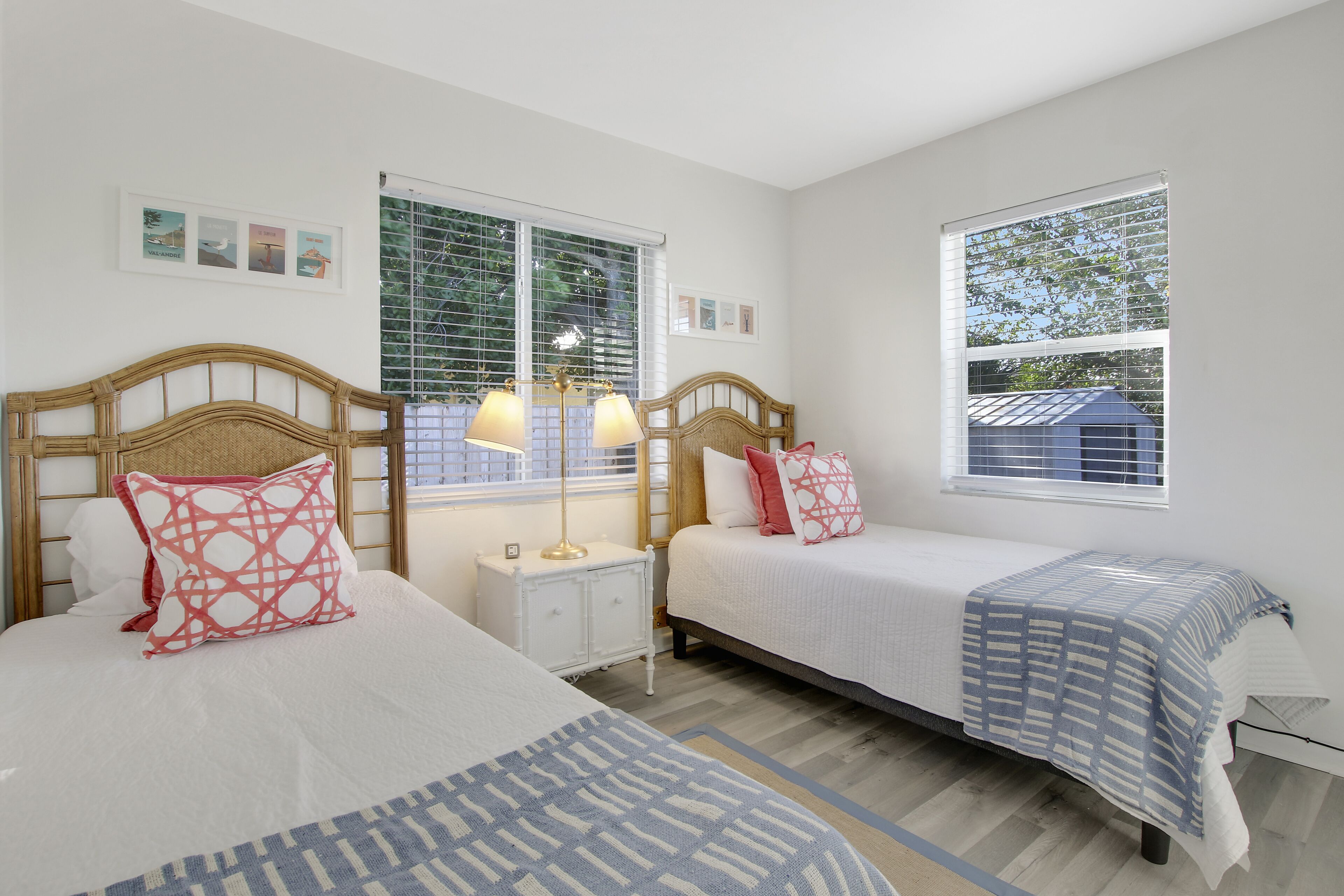 A hotel room with two beds, a nightstand, a lamp, and a window with blinds.