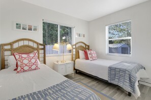 Une chambre d’hôtel avec deux lits, une table de chevet, une lampe et une fenêtre avec des stores.