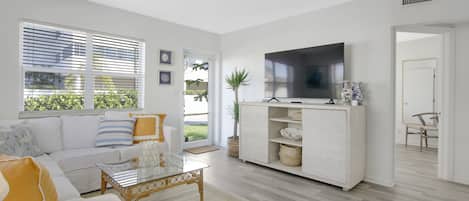 A modern living room with a sofa, coffee table, TV, and a large window with blinds.