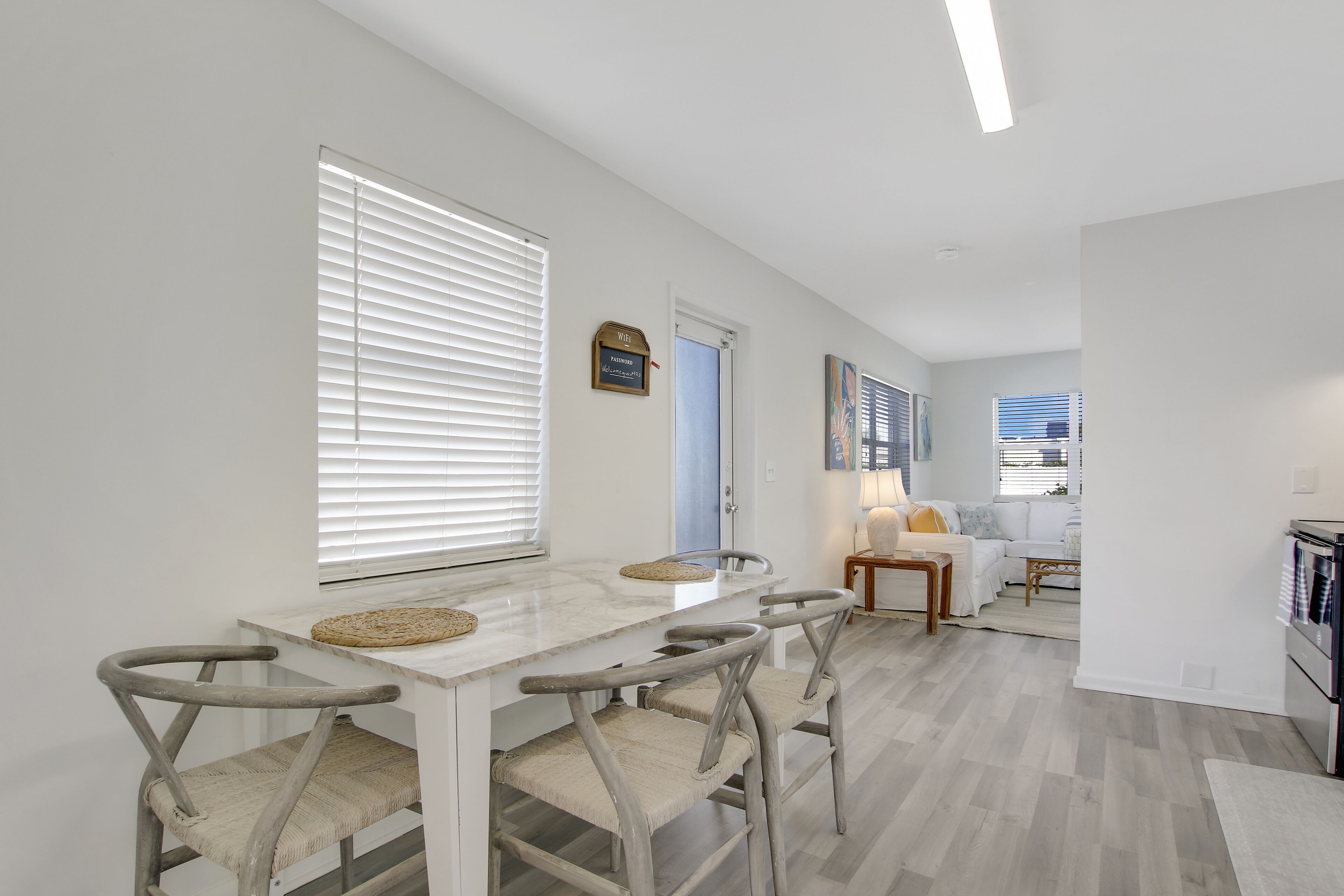 A modern kitchen with a marble countertop, four wooden chairs, and a dining table.