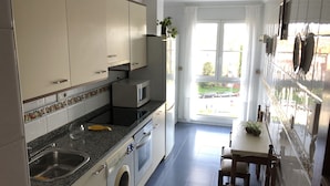 Et lille køkken med vaskemaskine, mikroovn og spiseplads med en stol og et bord.