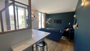 Un salon moderne avec une table blanche, un canapé bleu et un téléviseur fixé au mur.