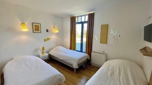 Une chambre avec deux lits simples, une petite table et une fenêtre avec des rideaux.
