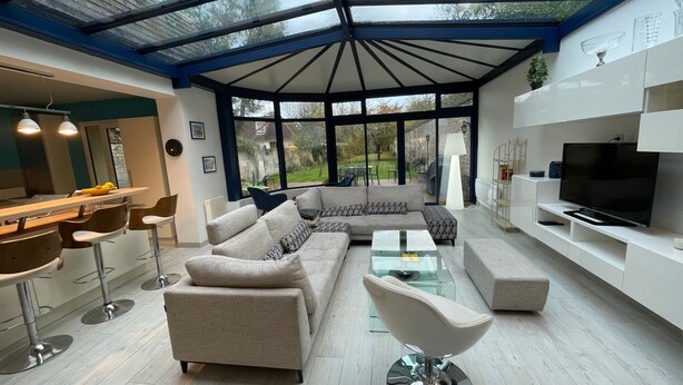 Ein modernes Wohnzimmer mit einer Glasdecke, einem Ecksofa, einem Glastisch und einem Fernseher auf einem weißen Schrank.