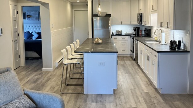 A modern kitchen with a central island, white cabinetry, and a dining area with two sofas. - Newly renovated 4BR & 3BR condo walk to slopes (Snowshoe)