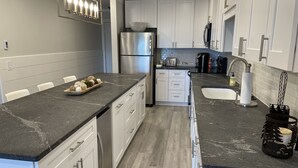 A modern kitchen with white cabinets, a stainless steel refrigerator, a built-in oven, and a granite countertop. - Newly renovated 4BR & 3BR condo walk to slopes (Snowshoe)