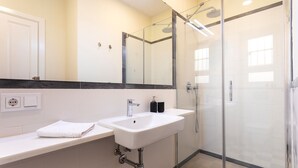 Et moderne badeværelse med en hvid vask, en glasbadeværelsesafskærmning og et stort spejl.