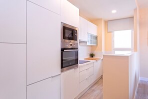A modern kitchen with white cabinetry, stainless steel appliances, and a window providing natural light.