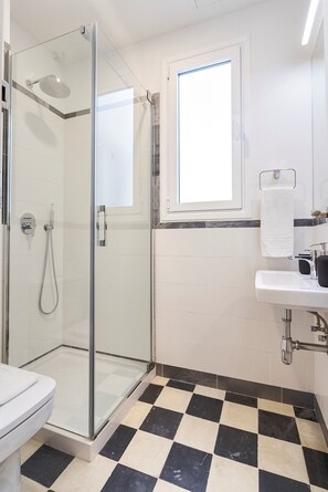 A bathroom with a glass-enclosed shower, a white sink, and a checkered floor.