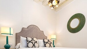 Uma cama bem arrumada com cabeceira, duas mesas de cabeceira com abajures, um tapete estampado e um ornamento circular na parede.
