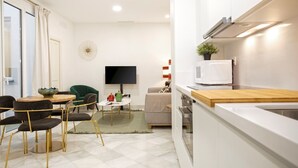 Uma sala de estar moderna com área de jantar, televisão de tela plana, cozinha com micro-ondas e uma cadeira verde.