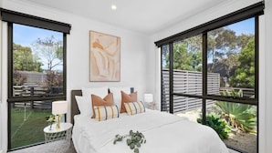 A bedroom with a large bed, two bedside tables, a nightstand, a window with a view of the outdoors, and a painting on the wall.