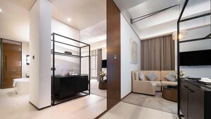 A modern living room with a sofa, a coffee table, and a TV. There is a kitchen area with a black countertop and cabinets. - Guigang Railway Station UEASY Hotel (Guigang)