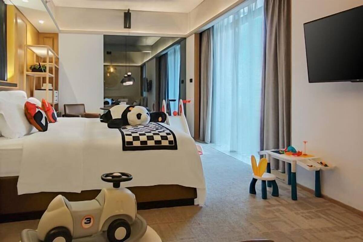A hotel room with a bed, a TV, a desk, and a window with curtains.