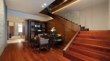 A modern interior with a wooden staircase, a dining area with chairs and a table, and a bookshelf.