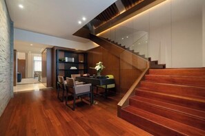Interior moderno com escada de madeira, área de refeições com cadeiras e mesa, e uma estante de livros.