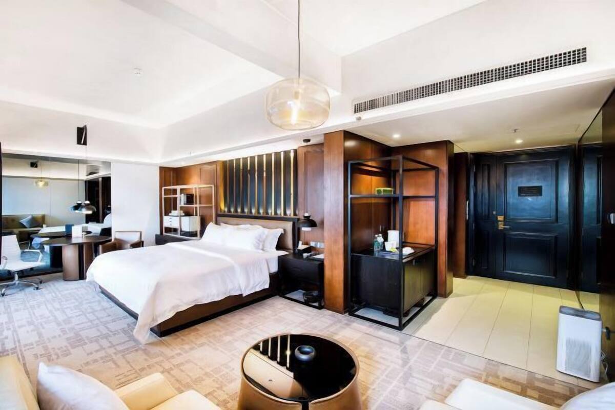 A modern hotel room with a large bed, a desk, a chair, a sofa, and a unique circular seating area.
