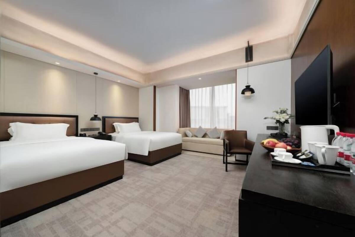 A hotel room with two beds, a sofa, a dining table with breakfast items, and a TV.