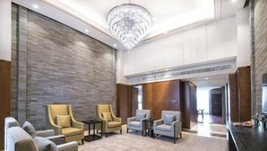 A spacious lobby with a modern chandelier, comfortable seating, and a large stone wall. - Guigang Railway Station UEASY Hotel (Guigang)