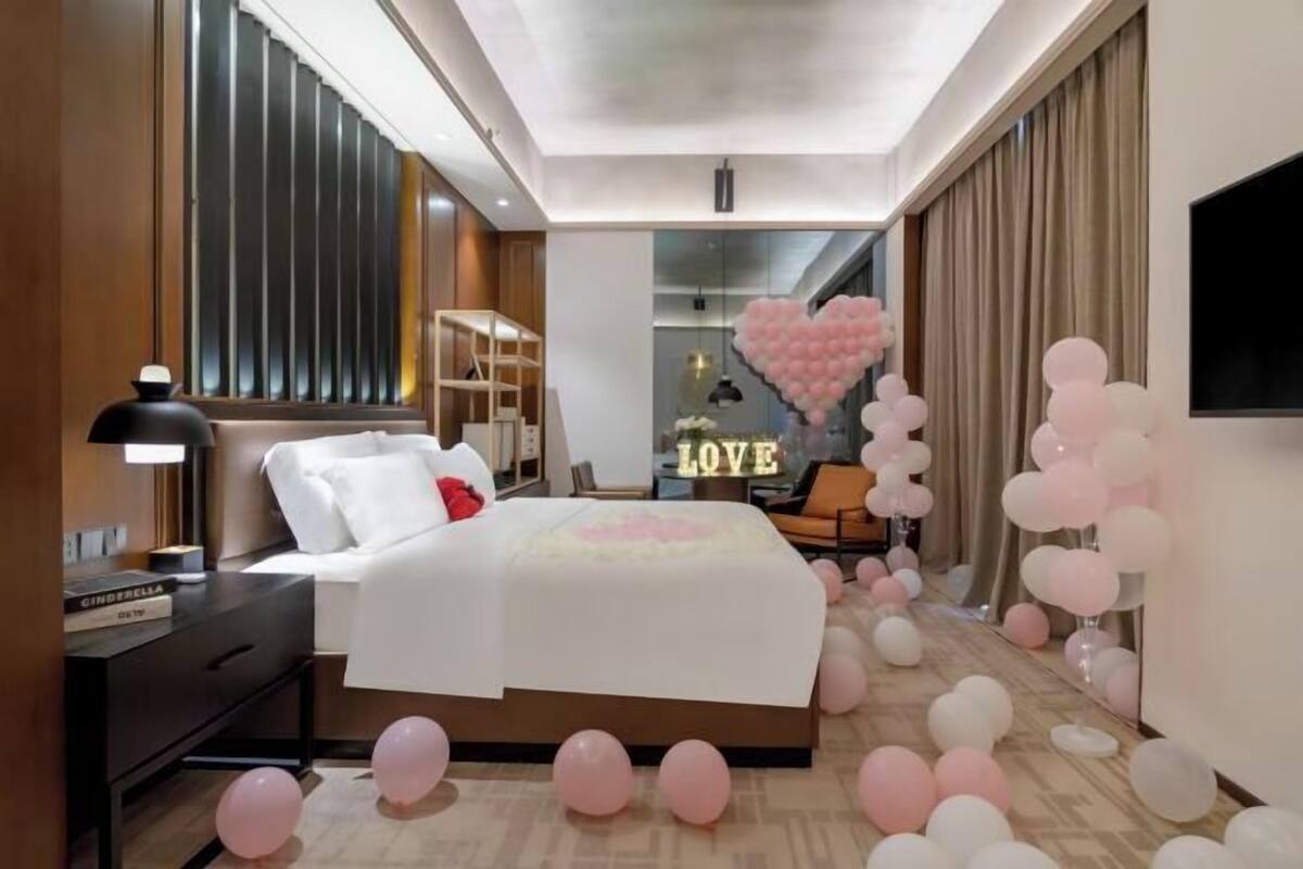 A modern hotel room with a large bed, a bedside table, a lamp, and a view of the city through the window.