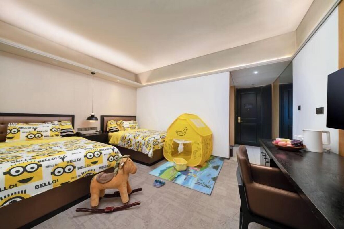A hotel room with two beds, a yellow playhouse, a rocking horse, and a dining area with a coffee maker.