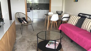 Um espaço de estar compacto com cozinha compacta, área de refeições, sofá e mesa de centro de vidro.
