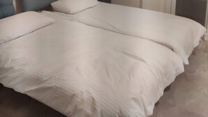 Um quarto com cama, almofadas, mesa de cabeceira, abajur e um quadro na parede.