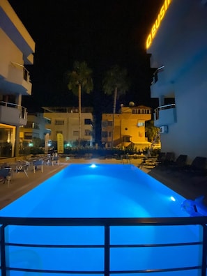 A nighttime view of a swimming pool with a blue-lit water feature, surrounded by buildings with balconies and outdoor seating. - Q Business Hotels (Antalya)