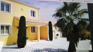 A yellow building with a tiled roof, a covered entrance, and a paved driveway. - Bright villa - Private pool - Near Pézenas (Valros)