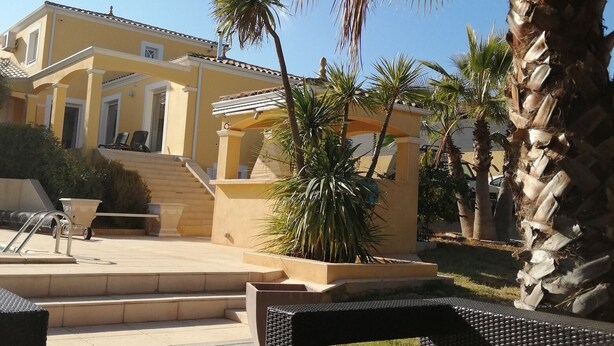 A courtyard with a pool, outdoor seating, palm trees, and a building with steps leading to a covered area. - Bright villa - Private pool - Near Pézenas (Valros)