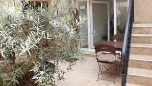 A patio with a table and chairs, a small olive tree, and a staircase leading to a glass door.
