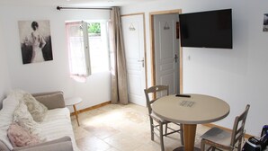 A room with a sofa, a small round table with chairs, a television mounted on the wall, and a door leading to another room.