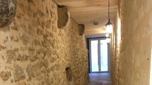 A narrow stone-walled corridor with a tiled floor and a black mat at the end.