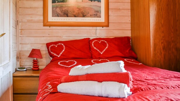 Ein Schlafzimmer mit einer Holzwand, einem gerahmten Gemälde, roter Bettwäsche, herzförmigen Kissen und einer roten Lampe.