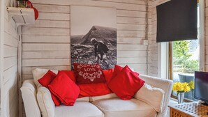 Ein gemütliches Zimmer mit einem weißen Sofa, roten Kissen und einem schwarzen Fernseher auf einem Holzschrank.