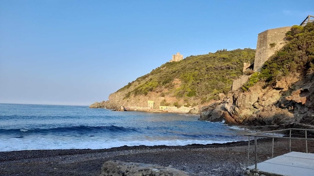 Ein felsiger Strand mit einem kleinen Gebäude auf einem Hügel mit Blick auf das Meer.