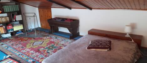 Ein Zimmer mit Hochladerbett, einem kleinen Tisch, einem Bücherregal und einem farbenfrohen Teppich.