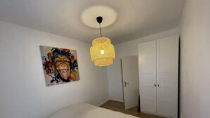 A bedroom with a bed, a bedside table, a hanging light fixture, a door, and a closet. - Newly renovated apartment, a stone's throw from town center and station (Strasbourg)