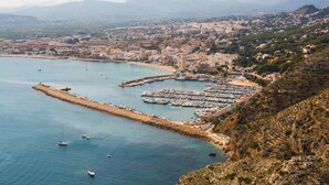 Un paisaje urbano costero con un puerto deportivo, barcos y montañas al fondo.