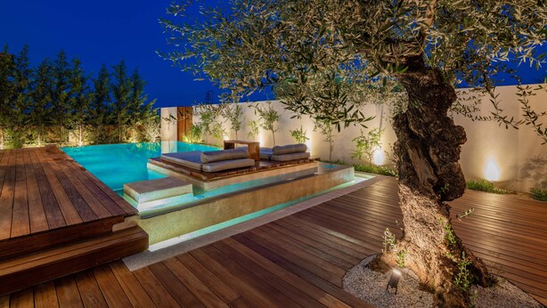 A wooden deck with a swimming pool, outdoor seating, and a large tree. - Oresteia Executive Villa, a Flamboyant Retreat (Tragaki)