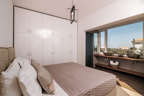 A bedroom with a large bed, white wardrobe, and a view of the sea through a window.