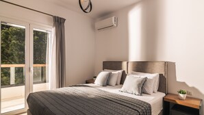 A modern bedroom with a large bed, a nightstand, a potted plant, and a sliding glass door leading to a balcony. - Oresteia Executive Villa, a Flamboyant Retreat (Tragaki)
