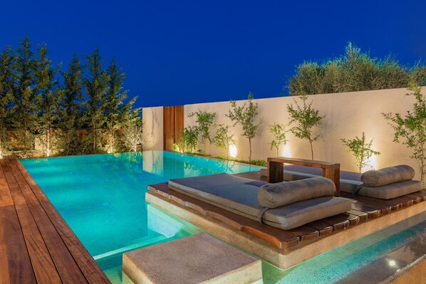 A serene outdoor pool area with wooden deck and lounge chairs.