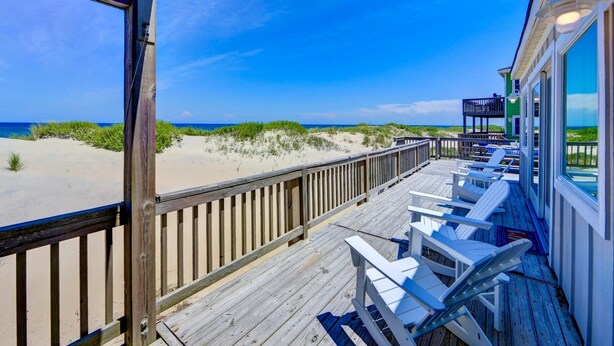 Een houten terras met witte stoelen met uitzicht op een strand.