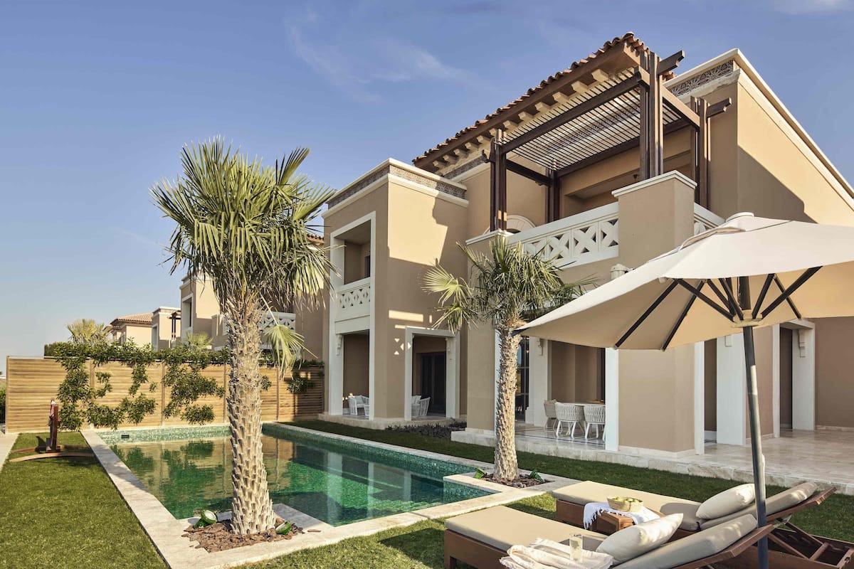 A modern two-story house with a swimming pool, outdoor seating, and palm trees.