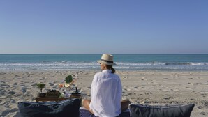 A person sitting on a beach chair with a table of food and drinks in front of them, overlooking the ocean. - Club Privé by Rixos Saadiyat Island (Abu Dhabi)