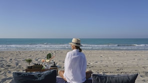 A person sitting on a beach chair with a table of food and drinks in front of them, overlooking the ocean. - Club Privé by Rixos Saadiyat Island (Abu Dhabi)