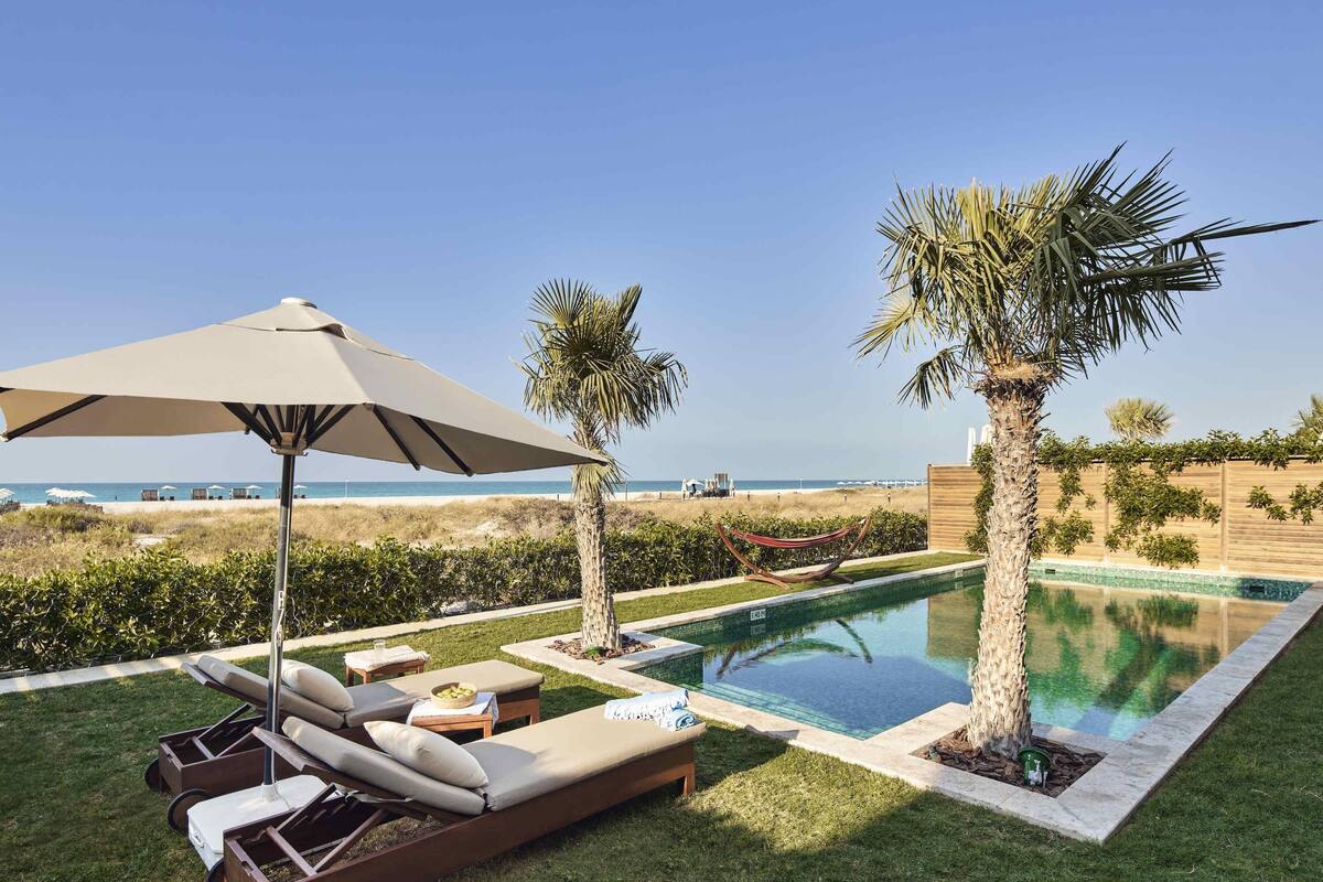 Ein Poolbereich mit Liegestühlen, einem großen Sonnenschirm und Blick auf den Strand.