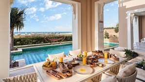 A dining area with a view of a pool and beach, featuring a table set with breakfast and a hammock in the background. - Club Privé by Rixos Saadiyat Island (Abu Dhabi)